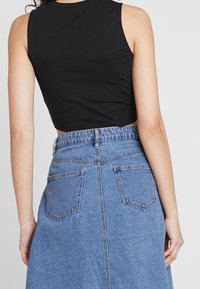 Top corto negro sin mangas combinado con una falda de mezclilla azul de cintura alta. La falda cuenta con dos bolsillos traseros y un ajuste relajado.