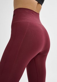 Hochgeschnittene bordeauxfarbene Leggings aus dehnbarem Stoff mit strukturierten Details an den Seiten und einer glatten Oberfläche am Bund.