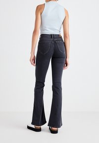 Top sin mangas de un azul claro ajustado con un cuello alto, combinado con pantalones vaqueros de tiro alto y acampanados de lavado oscuro que cuentan con bolsillos traseros y costuras en contraste.