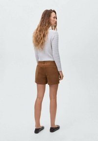 Suéter texturizado gris claro, pantalones cortos de ante marrón y zapatos negros de estilo slip-on, vistos desde atrás, destacando los colores y materiales del conjunto.