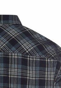 Kraag van een blauw en zwart geruit overhemd met een ruitpatroon. Katoenen stof met een gestructureerd oppervlak en contrasterende lichte lijnen.