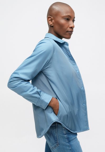 Lichtblauwe geknoopte blouse, gemaakt van gladde stof met een kraag, lange mouwen en een afgeronde zoom. Beschikt over zijzakken en een relaxte pasvorm.