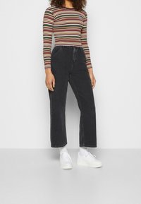 Langärmliges, gestreiftes Oberteil in Grün, Rot und Weiß, kombiniert mit hochsitztenden, lockeren schwarzen Jeans und weißen Plateausneakern.