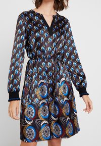 Robe à manches longues, noire à motifs, avec un décolleté en V, une taille froncée et des motifs circulaires vibrants en bleu, rouge et or avec des accents graphiques.