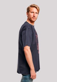 Dark blue cotton t-shirt with short sleeves, featuring a red graphic design on the front. Hemline sits just below the waist.