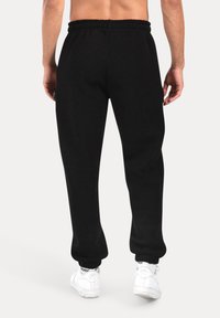 Sorte sweatpants med elastisk talje og manchetter ved anklerne, parret med hvide sneakers. Glat struktur og afslappet pasform.