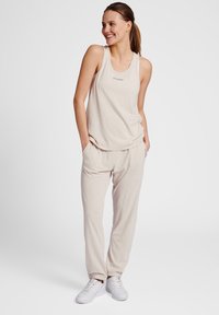 Light beige tank top and matching joggers made from soft fabric. Joggers have side pockets and fitted cuffs. White sneakers complete the outfit.