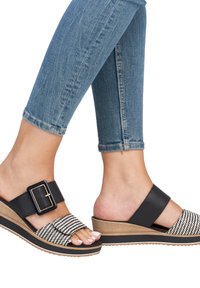 Schwarze und weiße Sandalen mit Absatz im geflochtenen Muster, ausgestattet mit einem breiten schwarzen Riemen, einer dekorativen Schnalle und einer Plattformsohle aus hellem Holz.