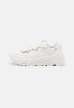 Hvid sneaker med et strømlinet design, der har mesh og syntetiske materialer, sølvdetaljer, en kraftig sål og traditionel snøring.