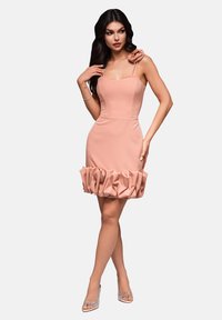 Robe rose ajustée avec des bretelles spaghetti, un ourlet en volants et un accent floral sur l'épaule, fabriquée à partir d'un tissu lisse et extensible.