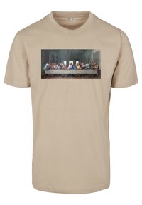 Beige katoenen t-shirt met een bedrukte afbeelding van de 'Laatste Avondmaal' en de tekst "JE KUNT NIET MET ONS MEESPELEN" onder de afbeelding.