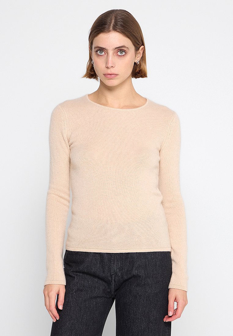 Hellbeige langärmliger Pullover aus weichem, strukturiertem Stoff mit Rundhalsausschnitt und tailliertem Schnitt, kombiniert mit dunklen Jeans.