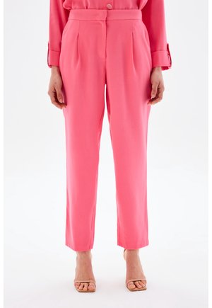 Femme portant un pantalon rose taille haute à jambes droites, associé à un chemisier rose assorti à manches longues et des escarpins beiges à bout ouvert.