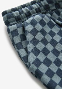 Gros plan d’un tissu à carreaux bleu et gris avec une ceinture élastique et des coutures visibles, probablement une partie d’une poche de vêtement.
