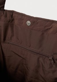 Hnědá látková taška s vnitřním zipovým kapsou a kovovým patentním uzávěrem blízko horního okraje.