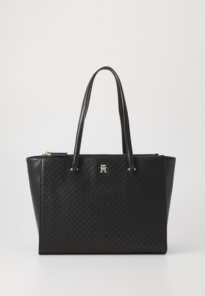 Zwarte tote bag met een textuurpatroon, leren handvatten, gouden hardware en een ritssluiting. Kenmerkt zich door een opvallend logo aan de voorkant.