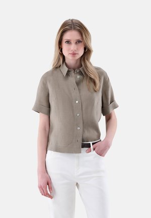 Beige Kurzarm-Hemd aus Leinen mit Kragen, rollbaren Ärmeln und kontrastierenden Knöpfen, kombiniert mit weißen Hosen.