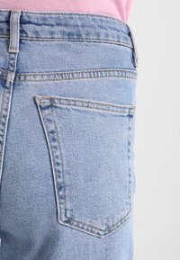 Vaqueros de mezclilla azul claro con un diseño ajustado. Las características destacadas incluyen bolsillos traseros, costuras sutiles y una textura desgastada.