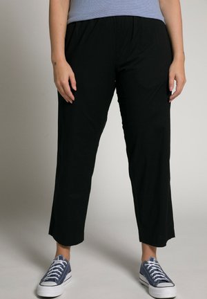 Schwarze, leichte, kurze Hosen mit elastischem Bund, kombiniert mit blauen Segeltuchschuhen mit weißen Schnürsenkeln und Gummisohlen.