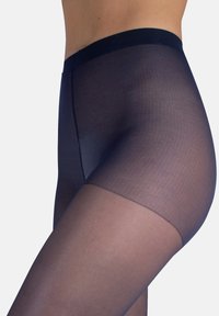 Nahaufnahme einer Person, die marineblaue durchsichtige Strumpfhosen trägt, mit Fokus auf der Hüfte und dem oberen Oberschenkelbereich vor einem schlichten Hintergrund.