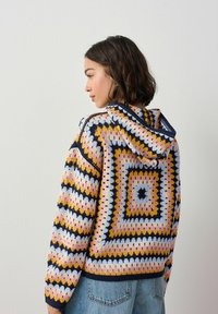 Kolorowa szydełkowana bluza z kapturem o geometrycznym wzorze w odcieniach różu, żółci, niebieskiego i granatowego. Posiada kaptur oraz prążkowane mankiety, teksturowany materiał.