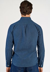 Camicia blu a maniche lunghe con colletto con bottoni, dettaglio piega posteriore e polsini con bottoni, realizzata in tessuto strutturato.