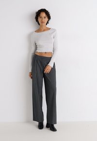 Pantalons gris à jambes larges associés à un haut court en maille ribbed gris clair à manches longues. Le tissu semble doux avec un ourlet brut. Bottes noires à la cheville.