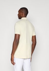 Beige polo shirt med korte ærmer og krave, der har subtile logodetaljer og en glat, let stofstruktur.