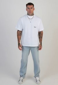 Bela bombažna majica s kratkimi rokavi in majhnim logotipom na prsih, kombinirana s svetlo modrimi kavbojkami iz jeansa in belimi supergami.