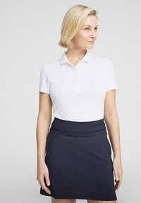 Biely polo tričko s golierom a radom gombíkov, v kombinácii s námorníckym modrým A-línie sukňou so širokým pásom. Hladký textilný povrch.