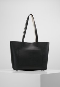 Svart läder tote-väska med två långa handtag, rektangulär form, platt framficka, slät textur och minimalistisk design.