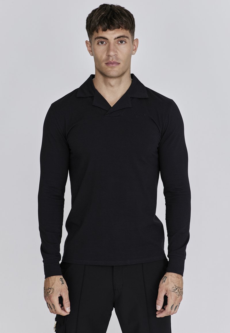 Camisa polo negra de manga larga con cuello en forma de V, textura suave y discreto logo. El corte es contemporáneo y ajustado.