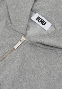 Szara bluza z kapturem na zamek, wykonana z miękkiego materiału. Posiada srebrny zamek błyskawiczny oraz wtopiony metkę z marką "BENU" w wyraźnym czarnym tekście.