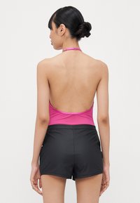 Maillot de bain rose à encolure halter avec un dos nu, associé à un short de bain noir. Le matériau semble lisse, ajusté et léger.