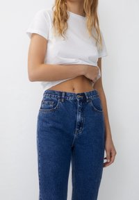 White cotton T-shirt with rolled sleeves, paired with high-waisted blue denim jeans featuring a classic five-pocket design and button closure.