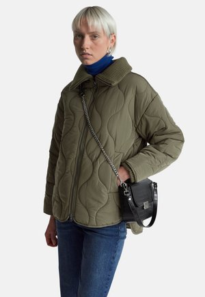 Kurtka w kolorze oliwkowym, pikowana, z prążkowanym kołnierzem, z zapięciem na zamek i bocznymi kieszeniami. W zestawie z czarną torbą na ramię w tłoczenie krokodyla.