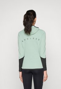 Lys grønn langermet hettegenser med svarte detaljer. Har teksten "ENDLESS" på baksiden, en hette og kontrastfargede teksturerte ermer.