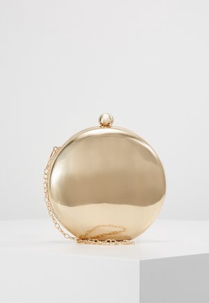 Bolso de mano redondo y brillante de color dorado con un cierre redondo y una cadena delgada dorada, descansando sobre una superficie blanca.