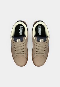 Beige skate shoes with a suede finish, featuring a tan rubber sole, navy colored accents, and black insoles with "etnies" branding.