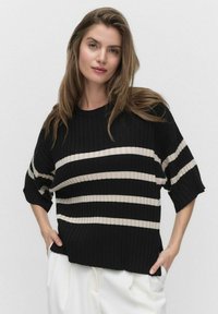 Zwart en crème gestreepte pullover, geribbelde textuur, brede mouwen, ronde halslijn en een relaxte pasvorm. Gecombineerd met witte broeken.