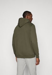 Olivengrøn hættetrøje med snøre i hætten, ribbede manchetter og kant. Båret med lysegrå sweatpants. Glat stofstruktur.