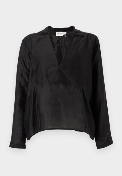 Blouse noire à manches longues avec un col en V, réalisée en tissu léger. Présente une coupe ample, un détail noué à l'avant et une surface légèrement texturée.