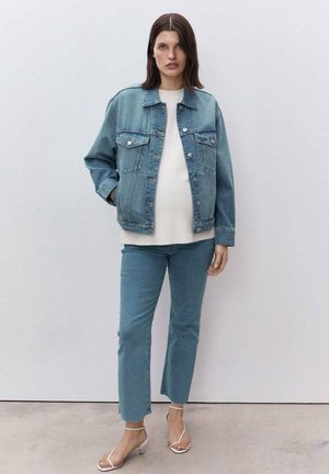Light blue denim jacket with a relaxed fit, worn over a cream top. Paired with light blue straight-cut jeans and clear heeled sandals.