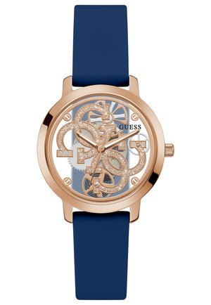 Guess watch featuring a rose gold bezel, blue silicone strap, and transparent dial with glittery logo and mechanical details.