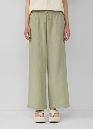 Pantalons larges vert clair en tissu texturé avec une taille élastique et un cordon de serrage. Associés à des sandales à plateforme.