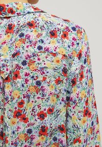 Floral-patterned blouse featuring a variety of multi-colored flowers on a light background, with a button-down front and patch pocket.