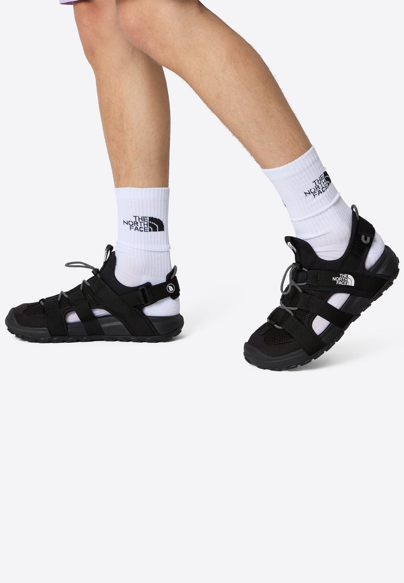 Black sport sandals with mesh and rubber materials, featuring adjustable straps and rubber soles, paired with white branded socks.