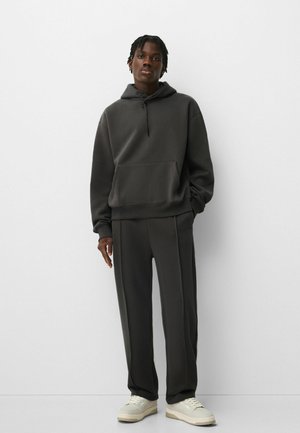 Dark gray hoodie with a kangaroo pocket, matching gray pants, and white sneakers. Fabric appears soft, with a relaxed fit and minimal design.