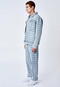 Veste en denim léger et pantalon assorti avec un motif géométrique, présentant un devant boutonné, deux poches et des baskets blanches.