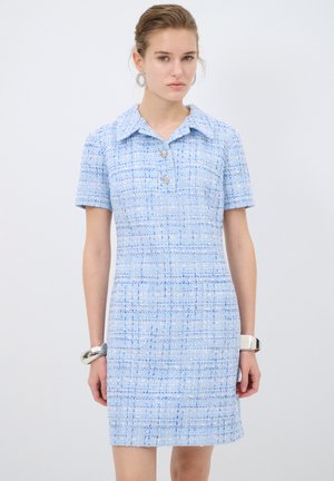 Kortärmad blauw jurk van gestructureerde stof, met kraag, twee knopen en een getailleerd silhouet. Bevat subtiele lichte en donkere blauwe patronen.